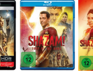 Der Superheld Shazam schaut in seinem roten Kostüm in die Kamera,. Vor seiner Brust der rote Schriftzug SHAZAM!. Im Hindergrund die Transparenten Gesichter von Nebendarsteler:innen